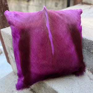 May include: A purple and brown cowhide pillow with a long, thin white stripe down the center. The pillow is soft and fluffy, and it would be a great addition to any home.