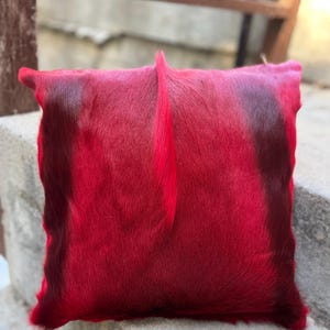 May include: Red cowhide pillow with a soft, fuzzy texture. The pillow is square shaped and has a subtle ombre effect.