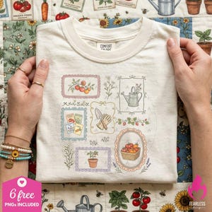 May include: A cream-colored t-shirt featuring a graphic print of various garden-themed illustrations enclosed in decorative frames, including tomatoes, a watering can, seed packets, a trowel, and a basket of harvested vegetables.