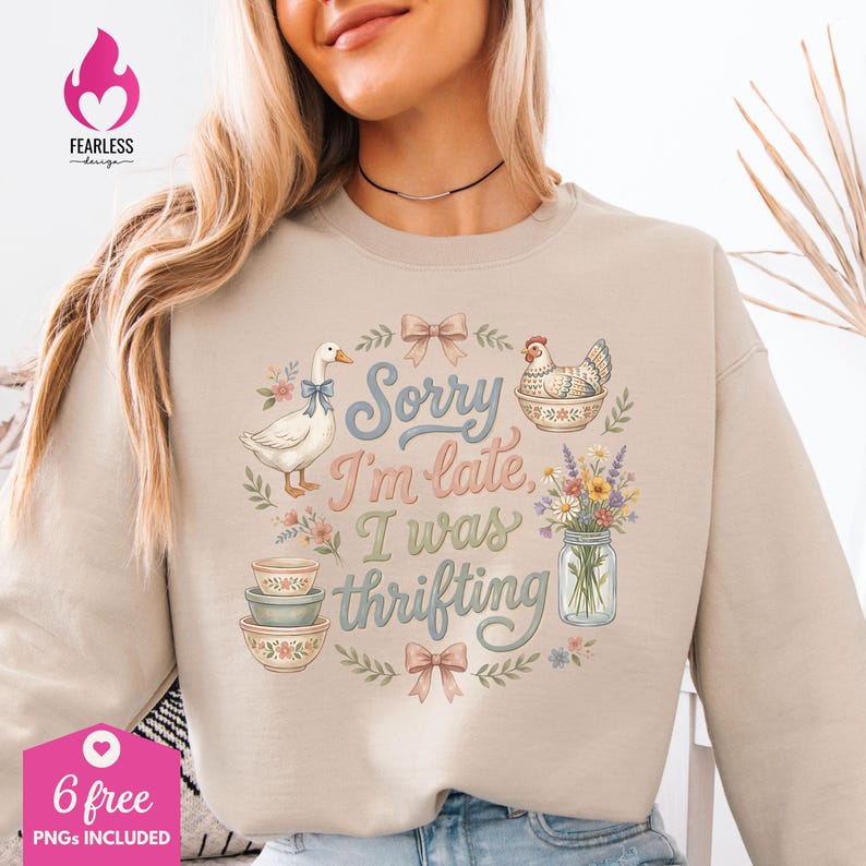 May include: Beige sweatshirt with a whimsical design featuring a goose, a chicken, floral elements, and the text "Sorry I'm late, I was thrifting." The design includes bows, bowls, and a jar of flowers.