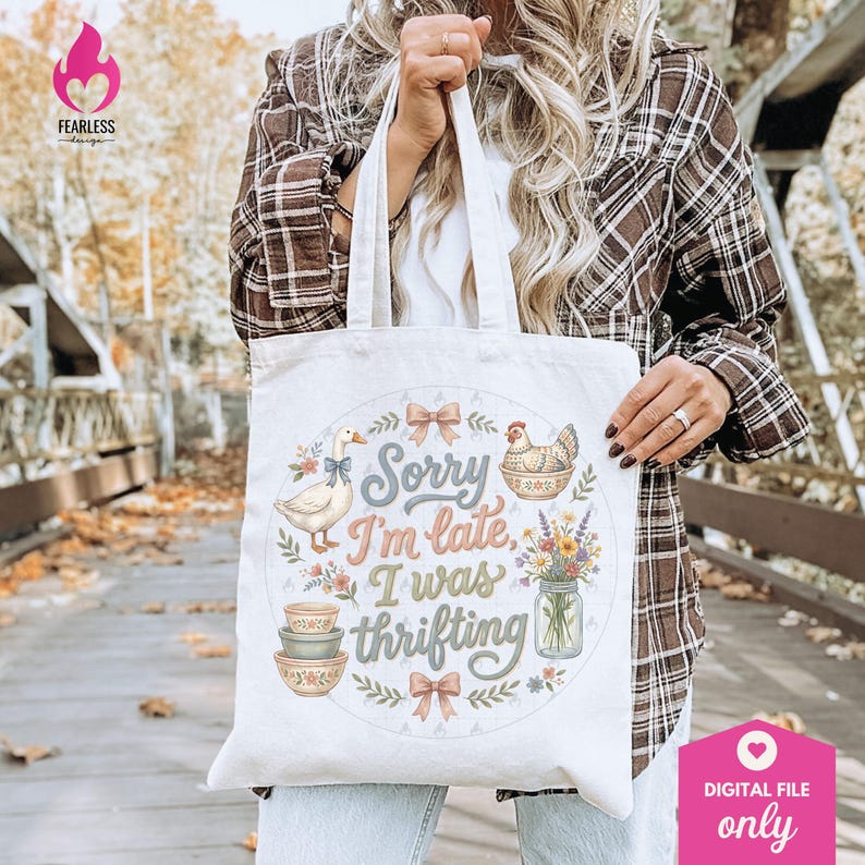 May include: Cream-colored tote bag with the text "Sorry I'm late, I was thrifting." The bag features illustrations of a goose, chicken, bowls, flowers, and bows. The bag is held by a person wearing a plaid shirt.