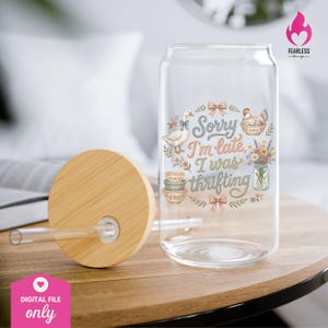 May include: A clear glass can-shaped drinking glass with a bamboo lid and straw. The glass features a whimsical design with a goose, chicken, bowls, flowers, and the text "Sorry I'm late, I was thrifting."
