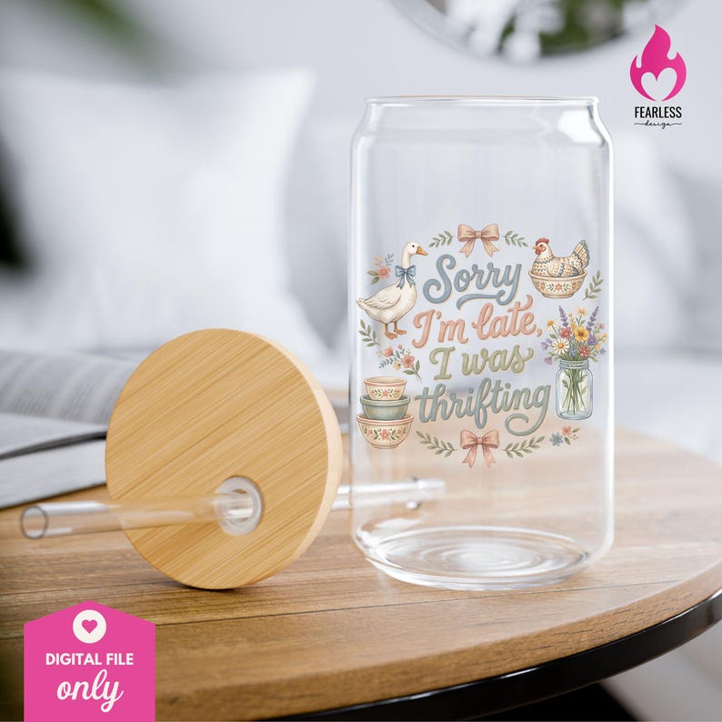 May include: A clear glass can-shaped drinking glass with a bamboo lid and straw. The glass features a whimsical design with a goose, chicken, bowls, flowers, and the text "Sorry I'm late, I was thrifting."
