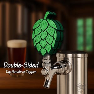 May include: A green hop-shaped tap handle or topper. The tap handle is double-sided and made of layered green material. The tap handle is attached to a stainless steel beer tap. The text "Double-Sided Tap Handle or Topper" is visible.