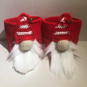 May include: Two red crocheted gnome-shaped Christmas stocking holders with white fur beards and white and red crocheted hats.
