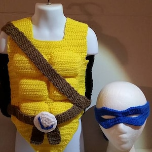 Peut inclure: Ensemble de costume de Tortue Ninja Adolescente Mutant crocheté, comprenant un gilet jaune et marron avec une ceinture et un masque pour les yeux bleu.