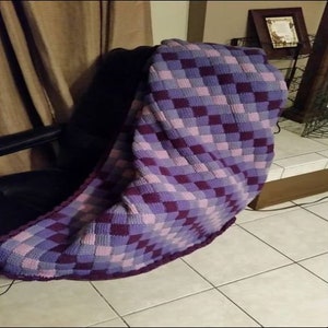 Puede incluir: Una manta de crochet a cuadros de color morado y rosa drapeada sobre una silla negra.