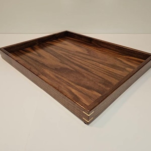May include: A rectangular wooden tray with a dark brown finish. The tray has a raised edge and is made of walnut wood. The edges of the tray are accented with thin strips of brass.
