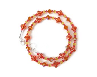 May include: A necklace featuring red and yellow beads. The necklace has a silver clasp and is composed of various sizes and shapes of beads. The larger beads are red with a white pattern, while the smaller beads are yellow and orange.