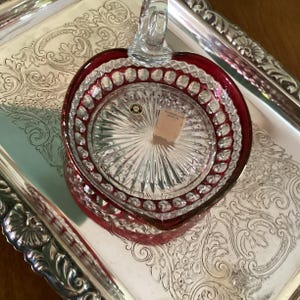 May include: A white ceramic mug with a black handle and the text "But First, Coffee" in a bold, black font. The mug is set against a blurred background, suggesting a cozy setting. The mug appears to be approximately 4 inches tall.