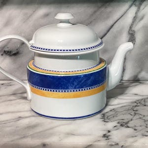 May include: A white teapot with a blue and yellow patterned design. The teapot has a lid and a spout.