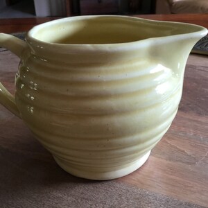 May include: A yellow ceramic pitcher with a ribbed design. The pitcher has a rounded body and a handle.