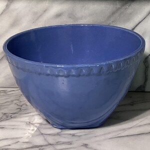 May include: A blue ceramic bowl with a slightly textured surface. The bowl has a rounded shape with a decorative rim. The bowl is likely used for serving food or as a decorative piece.