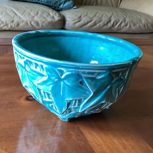 May include: A turquoise ceramic bowl featuring a raised relief pattern of ivy leaves on the exterior. The bowl has a glossy finish, a wide circular opening, and is supported by small feet at the base, showcasing a vibrant and uniform color throughout.