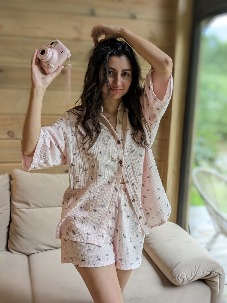 Peut inclure: Une femme portant un pyjama court rose et blanc &agrave; imprim&eacute; pissenlit. Elle tient un appareil photo instantan&eacute; rose dans sa main droite.