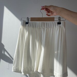 May include: White cotton shorts with a button fastening and a relaxed fit. The shorts are hanging on a wooden hanger.