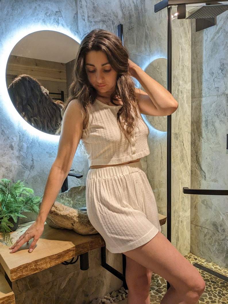 May include: A white ribbed tank top and matching shorts set. The top has a single button closure and the shorts have an elastic waistband.