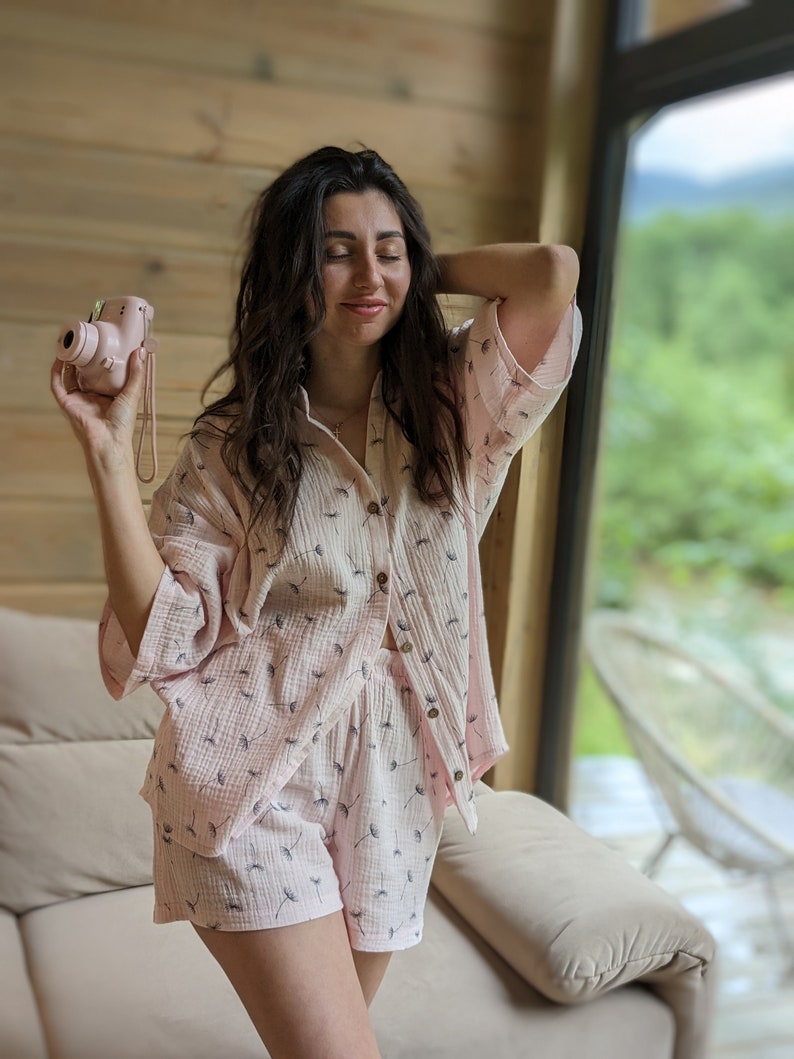 Peut inclure: Une femme portant un pyjama rose &agrave; imprim&eacute; pissenlit. L'ensemble de pyjama comprend une chemise &agrave; manches courtes et un short. Elle tient un appareil photo instantan&eacute; rose.