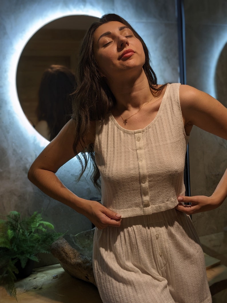 May include: A woman wearing a white, ribbed, button-up pyjama set. The set includes a sleeveless top and matching trousers.