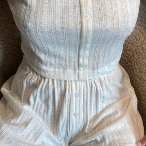 May include: White ribbed knit short set with a button-up top and matching shorts. The set has a relaxed fit and is made of a soft, comfortable fabric.
