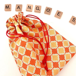 May include: A small orange and yellow drawstring bag with a red cord. The bag has a geometric pattern and the word "MANGOES" is spelled out with letter tiles.