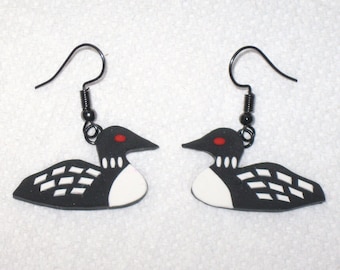 May include: A pair of black and white loon earrings with red eye details. The earrings feature a loon design with a black hook and a small black bead. The loon's body is white with black accents.
