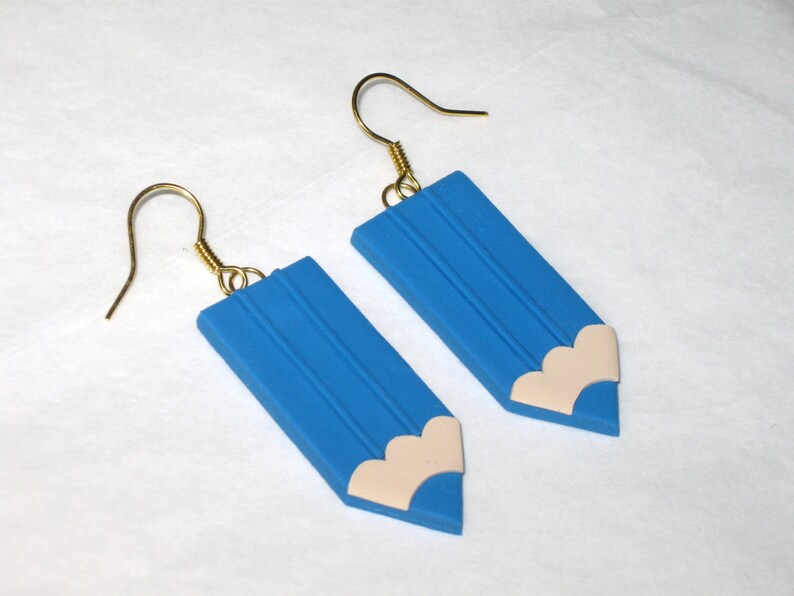 May include: A pair of blue pencil-shaped earrings with a white eraser detail. The earrings have gold hooks.