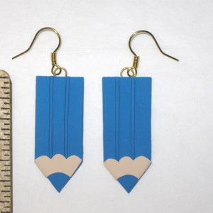 May include: A pair of blue pencil-shaped earrings with a white eraser detail. The earrings have gold hooks.