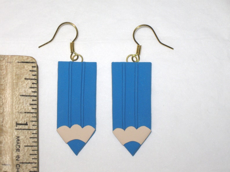 May include: A pair of blue pencil-shaped earrings with a white eraser detail. The earrings have gold hooks.