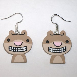 May include: A pair of brown and black cartoon squirrel earrings with a big toothy grin and pink nose. The earrings are made of polymer clay and have silver hooks.