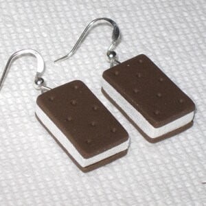 May include: A pair of silver dangle earrings with a brown and white ice cream sandwich charm. The charm is made of polymer clay and has a realistic look.