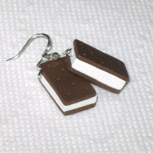 May include: A pair of silver dangle earrings with a chocolate and white ice cream sandwich charm. The charm is made of polymer clay and has a realistic look.