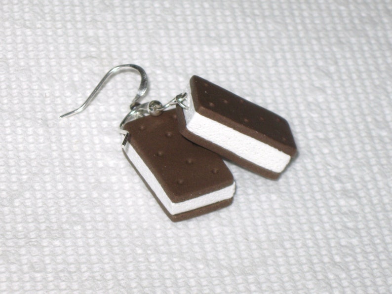 May include: A pair of silver dangle earrings with a chocolate and white ice cream sandwich charm. The charm is made of polymer clay and has a realistic look.