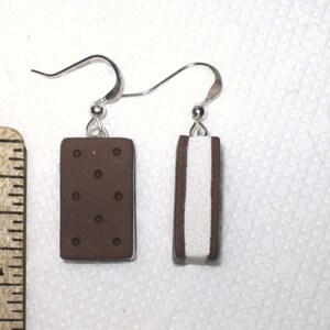 May include: A pair of earrings featuring a chocolate and vanilla ice cream sandwich design. The earrings are made of polymer clay and have silver hooks.
