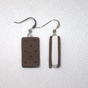 May include: A pair of earrings shaped like ice cream sandwiches. One earring is brown with white filling, and the other is white with brown filling.
