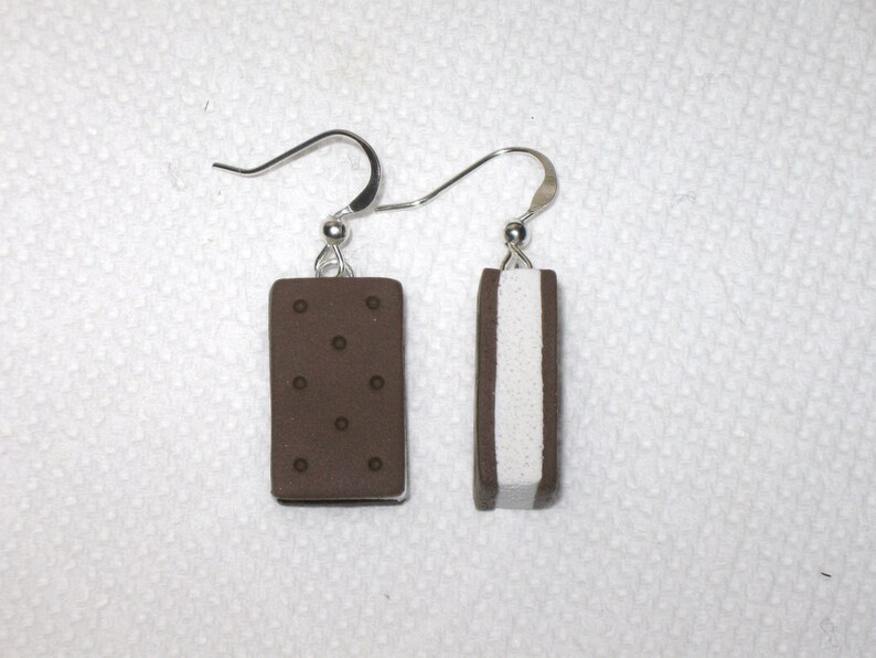 May include: A pair of earrings shaped like ice cream sandwiches. One earring is brown with white filling, and the other is white with brown filling.