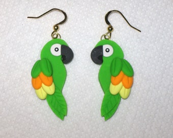 May include: A pair of green parrot dangle earrings with yellow and orange accents. The parrots have black eyes and beaks.