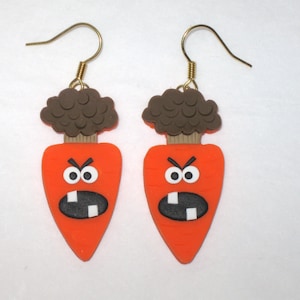 May include: A pair of orange carrot earrings with angry faces and brown hair. The earrings have gold hooks.