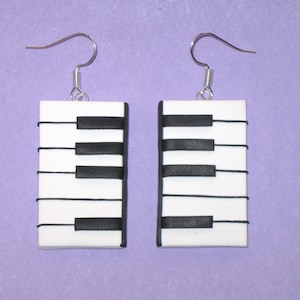 May include: A pair of white and black piano key earrings. The earrings are made of polymer clay and have silver hooks.