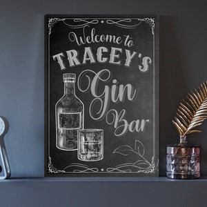 May include: Black chalkboard sign with white lettering that says "Welcome to Tracey's Gin Bar". The sign features a drawing of a bottle of gin and a glass of gin.