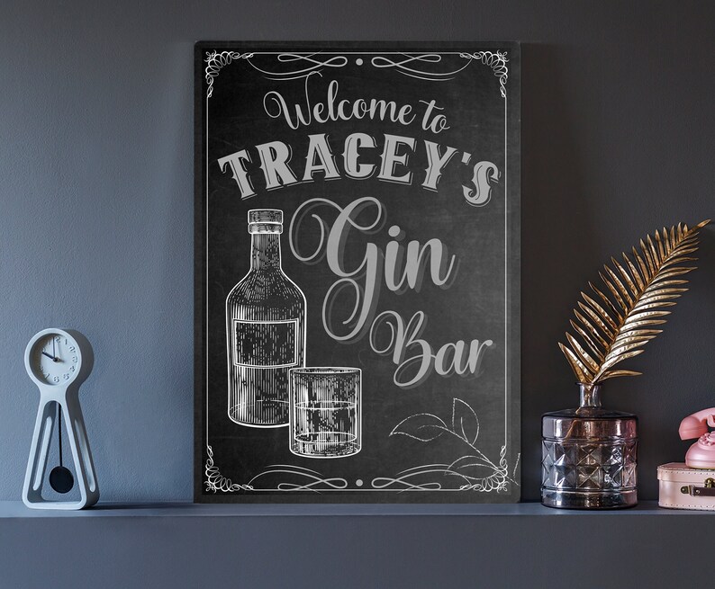 May include: Black chalkboard sign with white lettering that says "Welcome to Tracey's Gin Bar". The sign features a drawing of a bottle of gin and a glass of gin.