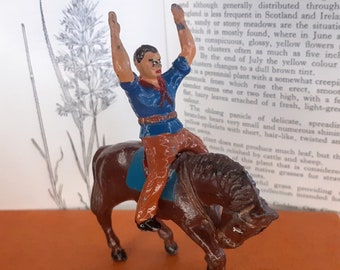 May include: A vintage toy figurine of a cowboy riding a brown horse. The cowboy is wearing a blue shirt, a red neckerchief, and brown trousers. The horse has a blue saddle.