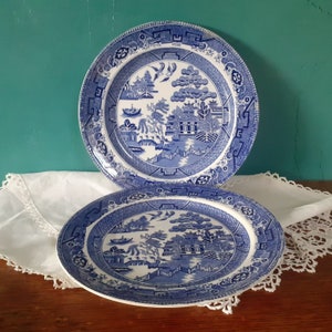 Puede incluir: Dos platos de cerámica azul y blanco con un diseño de sauce. Los platos tienen un fondo blanco con un sauce azul, un puente y una pagoda.