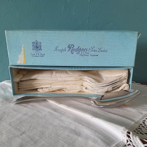 May include: A set of silver spoons in a light blue box. The box is labeled "Joseph Rodgers & Sons Limited, Sheffield, England." The spoons are resting on a white cloth. The box is open, revealing the spoons.