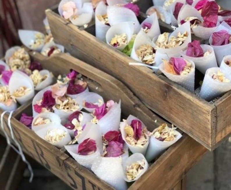 May include: Two wooden crates filled with white paper cones filled with dried flower petals. The cones are tied with twine and the petals are pink and white.