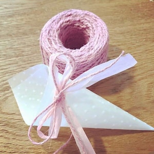 May include: A white paper cone with a pink polka dot pattern is tied with a pink ribbon and twine. The twine is wrapped around a spool.