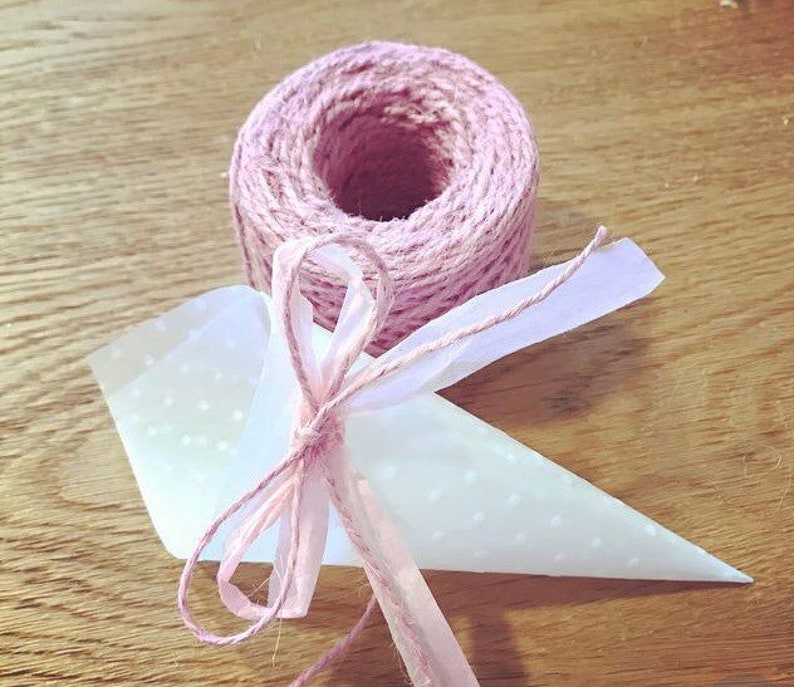 May include: A white paper cone with a pink polka dot pattern is tied with a pink ribbon and twine. The twine is wrapped around a spool.