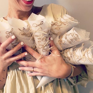 May include: A person holding a large bouquet of white paper cones tied with twine and decorated with small white polka dots.