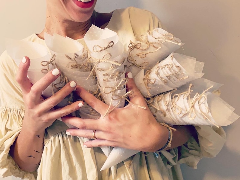 May include: A person holding a large bouquet of white paper cones tied with twine and decorated with small white polka dots.
