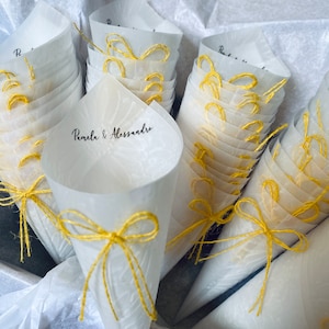 May include: A stack of white paper cones with yellow string bows. The cones are decorated with a delicate floral pattern and the text "Pamela & Alessandro".
